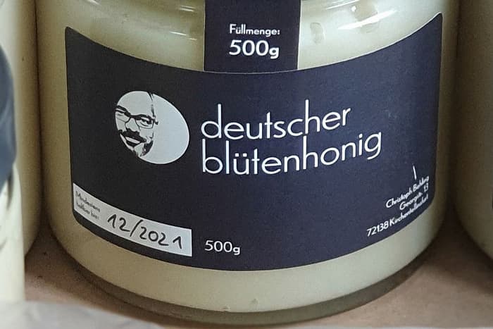 Nahaufnahme des Etiketts: eine runde Bildmarke mit dem Porträt des Imkers, daneben die Schriftzüge „deutscher blütenhonig“ und „Füllmenge: 500g“.